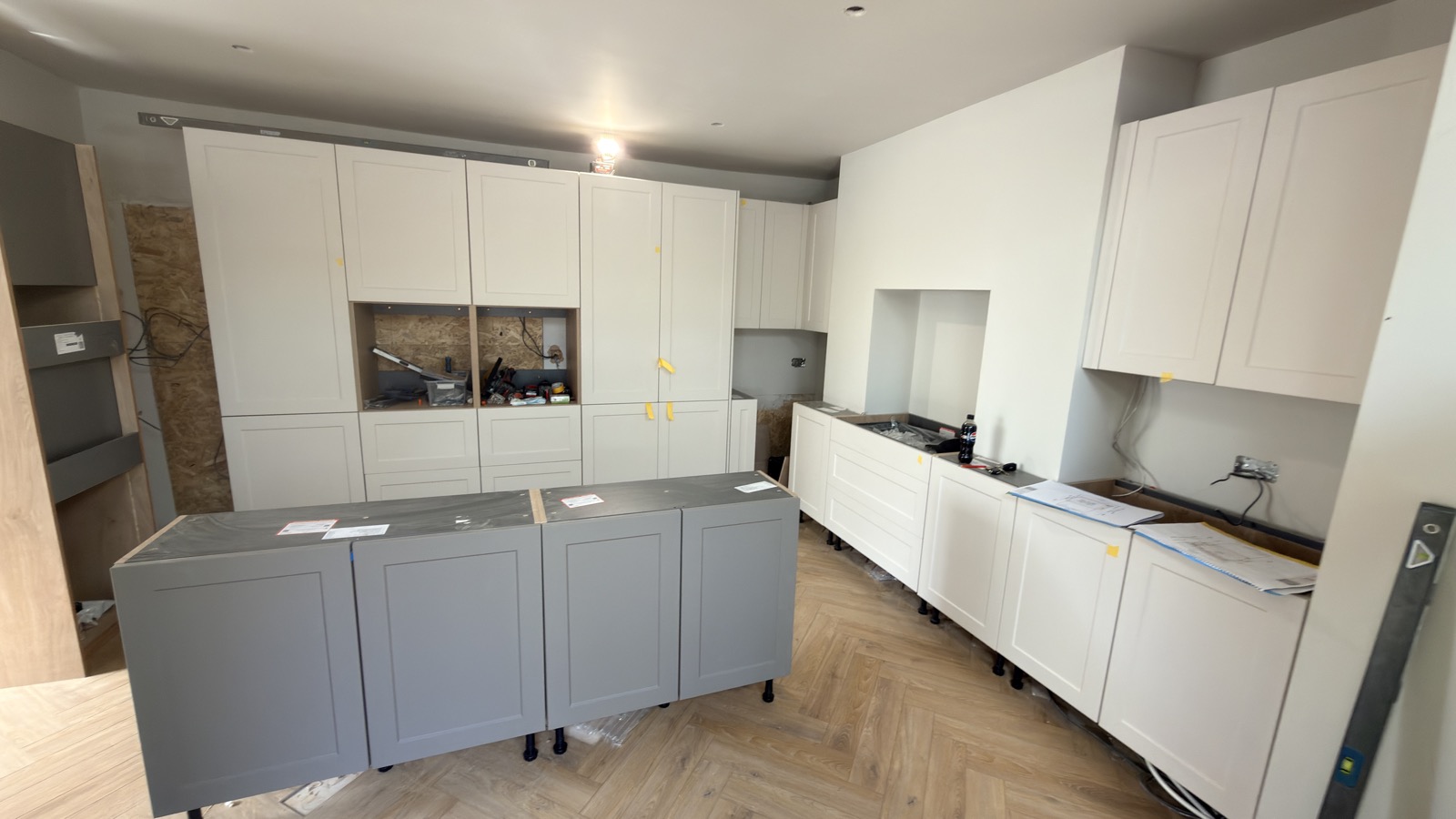 Shaker kitchen cabinetry and island during installation, with herringbone flooring